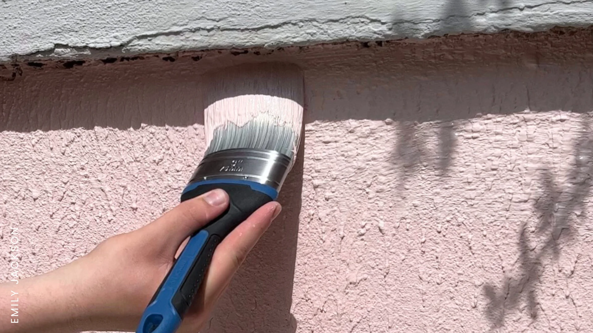 A brush applying pink masonry paint