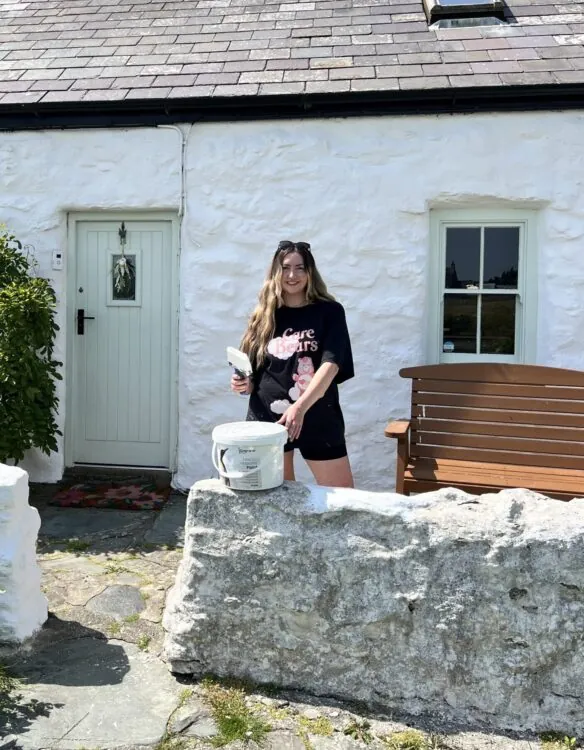 A girl stood outside her white house aftering painting it